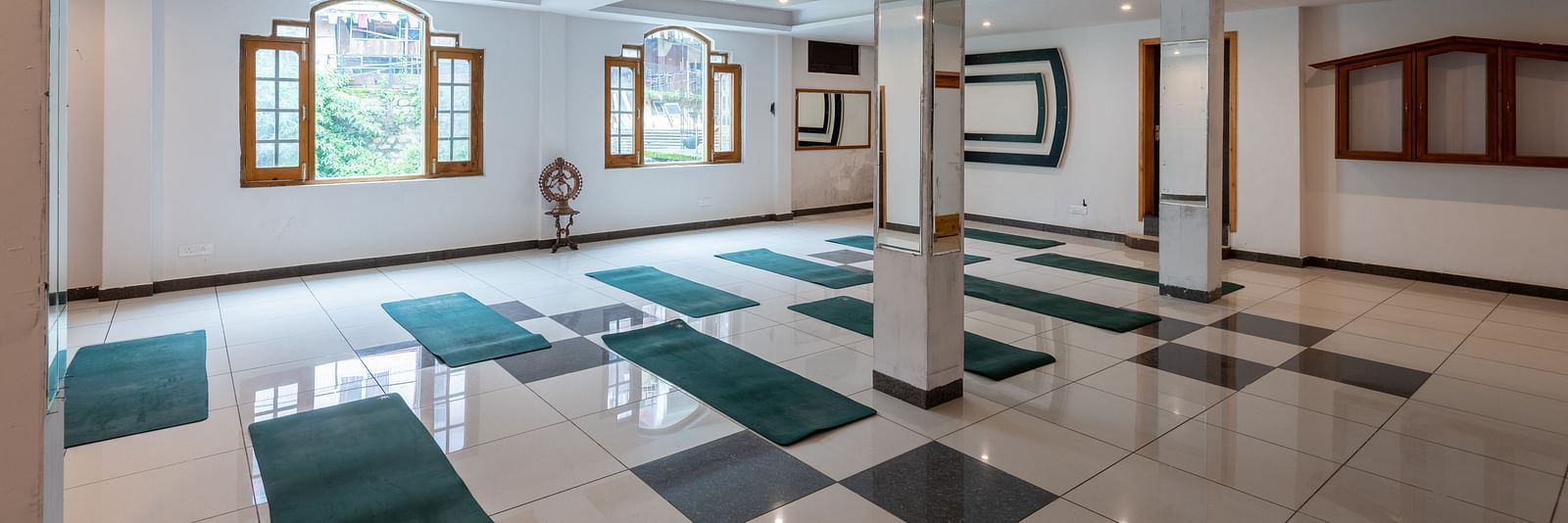 A spacious yoga studio with a tiled floor, large windows, and multiple green yoga mats laid out - DLS Meghavan Resort